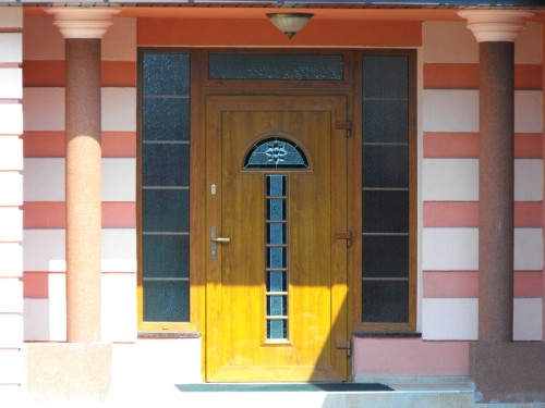 Drzwi PVC SCHÜCO, kolor złoty dąb z wypełnieniem wsadowym Adeco Opal i doświetleniami bocznymi.
